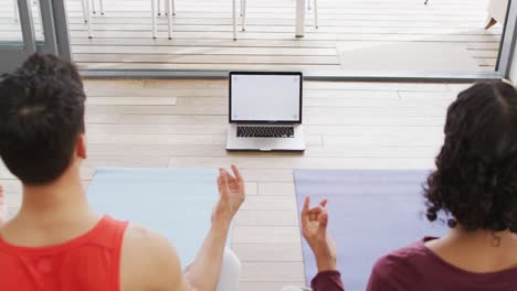 Happy-diverse-male-couple-doing-yoga,-meditating-using-laptop-with-copyspace-in-living-room