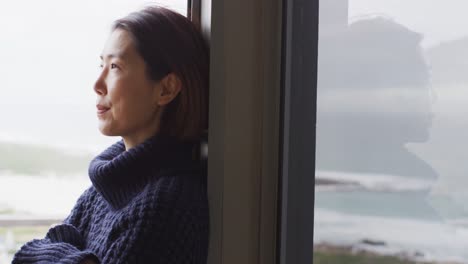 Glückliche-Asiatische-Frau-Mit-Pullover,-Die-Sich-Allein-Am-Fenster-Entspannt-Und-Denkt