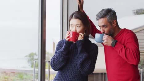 Happy-diverse-couple-drinking-coffee-and-talking-together-at-home