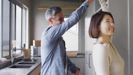 Happy-diverse-couple-holding-hands-and-dancing-together-in-kitchen