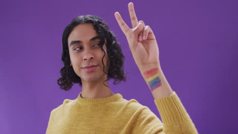 Portrait-of-happy-biracial-man-with-lgbt-flag-on-arm-on-purple-background