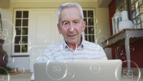 Animation-of-falling-5g-icons-over-caucasian-senior-man-using-laptop