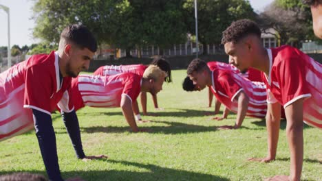 Diverse-group-of-male-football-players-warming-up-on-field,-doing-push-ups