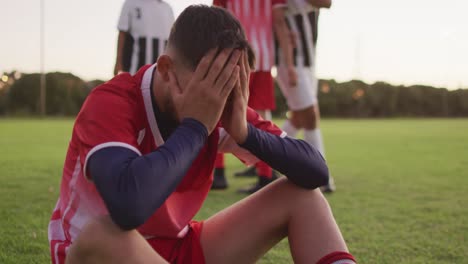 Video-Eines-Traurigen-Gemischtrassigen-Fußballspielers,-Der-Auf-Dem-Spielfeld-Sitzt