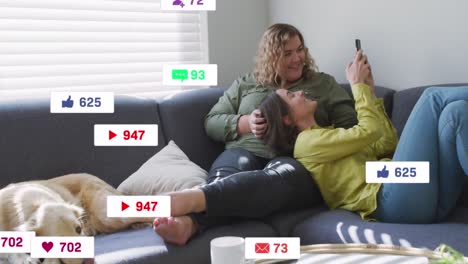 Animation-of-social-media-icons-falling-over-two-caucasian-women-using-smartphone