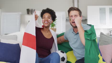 Video-De-Una-Feliz-Pareja-Diversa-Sosteniendo-Banderas-De-Portugal-E-Inglaterra-Y-Viendo-Partidos-En-Televisión
