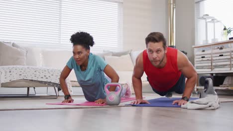Video-of-happy-diverse-couple-training-together-at-home,-doing-plank