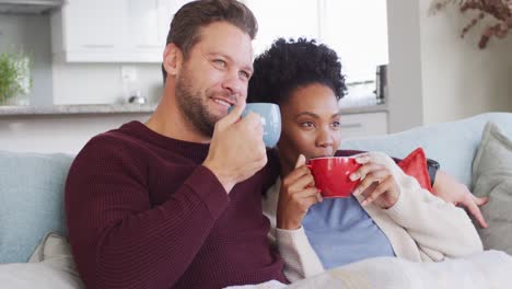 Video-Eines-Glücklichen,-Vielfältigen-Paares,-Das-Sich-Auf-Dem-Sofa-Umarmt-Und-Kaffee-Trinkt