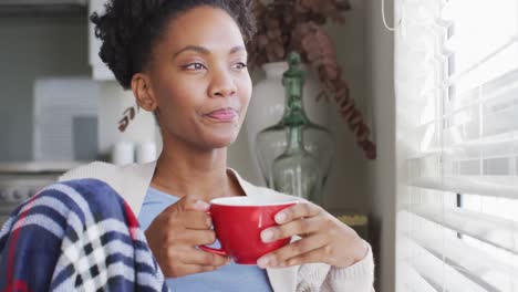 Video-of-thoughtful-african-american-woman-drinking-coffee-and-looking-outside-window