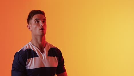 Kaukasischer-Männlicher-Rugbyspieler,-Der-Rugbyball-über-Orangefarbener-Beleuchtung-Fängt