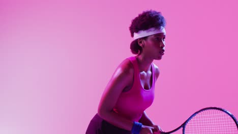 Video-of-focused-african-american-female-tennis-player-hitting-ball-on-neon-pink-lightning