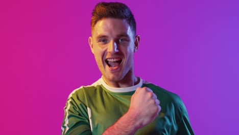 Portrait-of-happy-caucasian-male-soccer-player-raising-hands-over-neon-pink-lighting