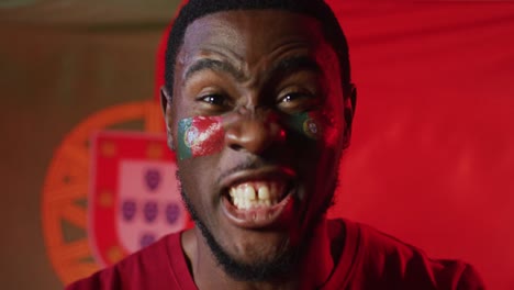 Porträt-Eines-Glücklichen-Afroamerikanischen-Männlichen-Fußballfans-Mit-Der-Flagge-Portugals-über-Rosafarbener-Beleuchtung
