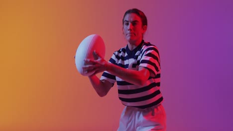 Kaukasische-Rugbyspielerin-Fängt-Rugbyball-über-Neonrosa-Beleuchtung