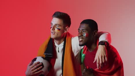 Fröhliche,-Vielfältige-Männliche-Fußballfans-Mit-Nationalflaggen-über-Rosafarbener-Beleuchtung