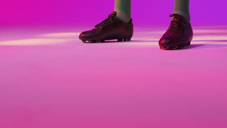 Male-soccer-player-with-football-over-neon-pink-lighting