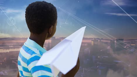 Animation-of-network-of-connections-over-african-american-boy-with-paper-plane-and-cityscape