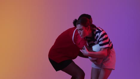 Diverse-female-rugby-players-playing-rugby-over-neon-pink-lighting