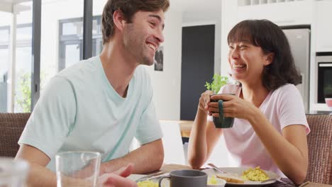 Video-Eines-Glücklichen,-Vielfältigen-Paares,-Das-Sein-Smartphone-Nutzt-Und-Gemeinsam-In-Der-Küche-Kaffee-Trinkt
