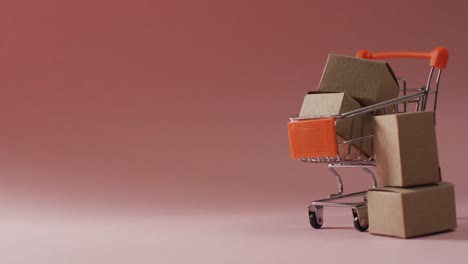 Video-of-shopping-trolley-with-cardboard-boxes-and-copy-space-on-pink-background