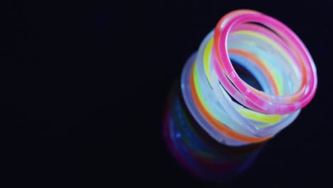 Animation-of-multiple-colorful-neon-glow-sticks-over-black-background-with-copy-space