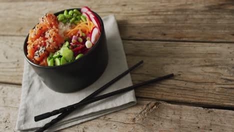 Composition-of-bowl-of-rice,-salmon-and-vegetables-with-chopsticks-on-wooden-background