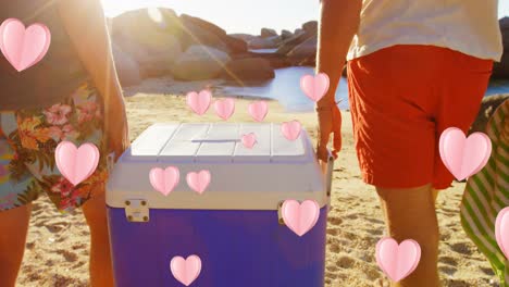 Animation-of-hearts-over-midsection-of-caucasian-men-with-tourist-fridge-on-beach