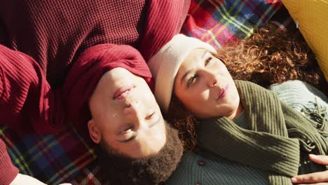 Video-of-biracial-couple-warmly-dressed-lying-on-blanket-spending-time-in-the-garden