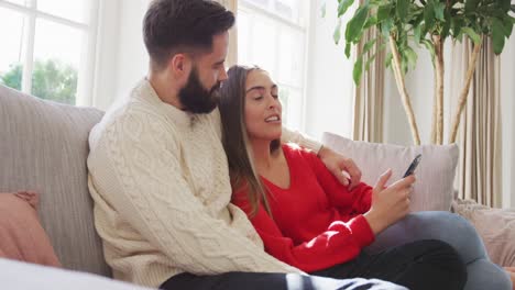 Video-of-happy-caucasian-couple-siting-on-sofa-and-using-smartphone