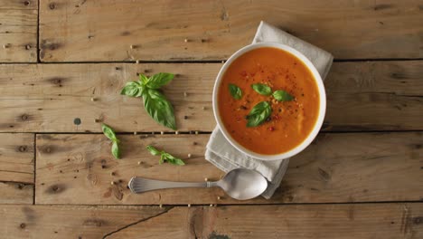 Video-of-cream-tomato-soup-in-bowl-on-wooden-table-with-basil-leaves
