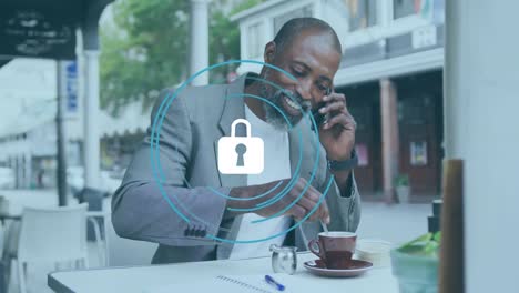 Animation-of-padlock-with-circles-over-african-american-man-talking-on-cellphone-and-mixing-coffee