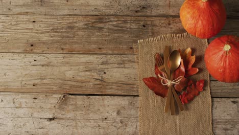 Video-of-cutlery,-cloth-and-autumn-decoration-with-pumpkins-lying-on-wooden-surface