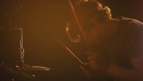 Video-of-caucasian-male-drummer-playing-drum-kit,-under-orange-coloured-lights