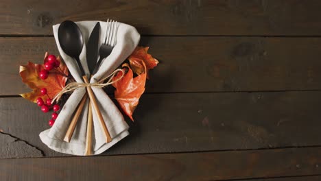 Video-of-cutlery,-cloth-and-autumn-decoration-lying-on-wooden-surface