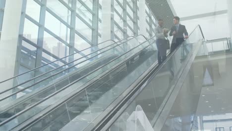 Diverse-male-business-colleagues-with-tablet-talking-on-escalator,-over-cityscape