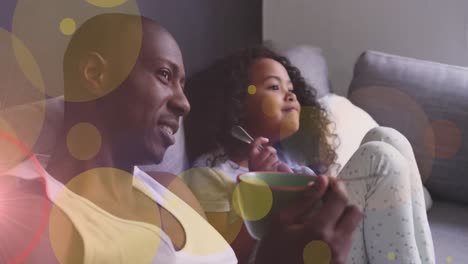 Animation-of-dots-moving-over-happy-african-american-father-and-daughter-eating-and-watching-tv