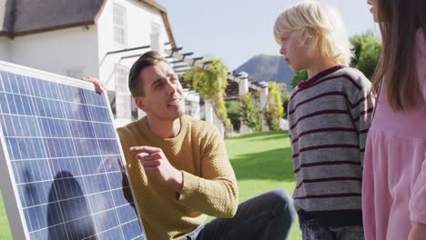 Video-of-happy-caucasian-father-explaining-solar-panel-to-son-and-daughter-in-sunny-garden