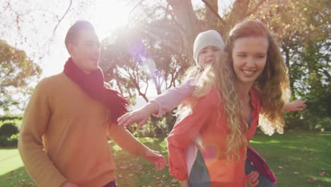 Video-of-happy-caucasian-parents,-smiling-mother-piggybacking-daughter-in-sunny-autumn-garden