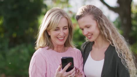 Video-of-happy-caucasian-senior-mother-and-adult-daughter-looking-at-smartphone-in-garden