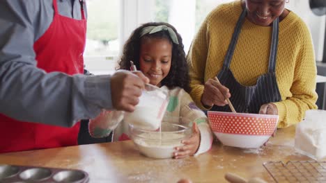 Video-of-happy-african-american-granddaughter-baking-with-grandparents-in-kitchen