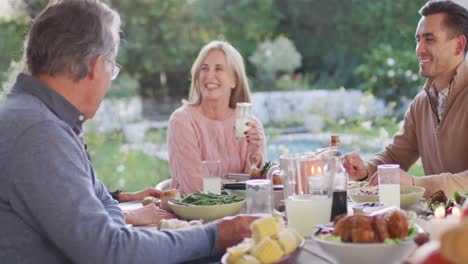 Video-of-happy-caucasian-parents,-daughter-and-grandparents-talking-at-outdoor-dinner-table