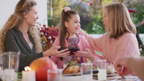 Video-of-happy-caucasian-mother-daughter-and-grandmother-looking-at-smartphone-at-dinner-table