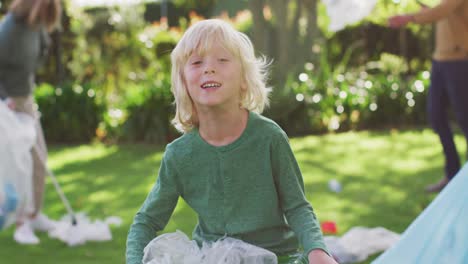 Retrato-En-Video-De-Un-Niño-Caucásico-Sonriente-Recogiendo-Plástico-Para-Reciclar-Con-Su-Familia-Al-Aire-Libre