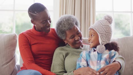 Video-Einer-Lächelnden-Afroamerikanischen-Mutter,-Tochter-Und-Großmutter,-Die-Auf-Dem-Sofa-Sitzen-Und-Sich-Umarmen
