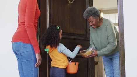 Video-of-happy-african-american-mother-and-daughter-trick-or-treating-at-grandmother's-house