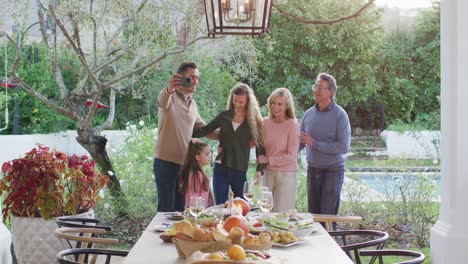 Video-of-happy-caucasian-parents,-daughter-and-grandparents-taking-selfie-at-outdoor-family-dinner