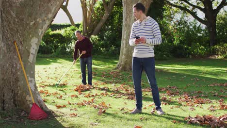 Video-of-happy-caucasian-senior-father-and-adult-son-gardening-and-looking-at-smartphone