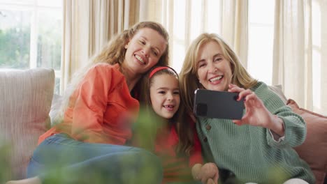 Video-of-happy-caucasian-mother-and-grandmother-taking-selfie-with-granddaughter-on-couch