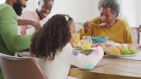 Video-of-happy-african-american-parents,-daughter-and-grandparents-eating-at-dinner-table