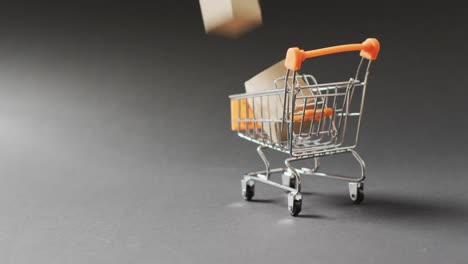 Shopping-trolley-with-cardboard-box-inside,-on-seamless,-lit-black-background-with-copy-space